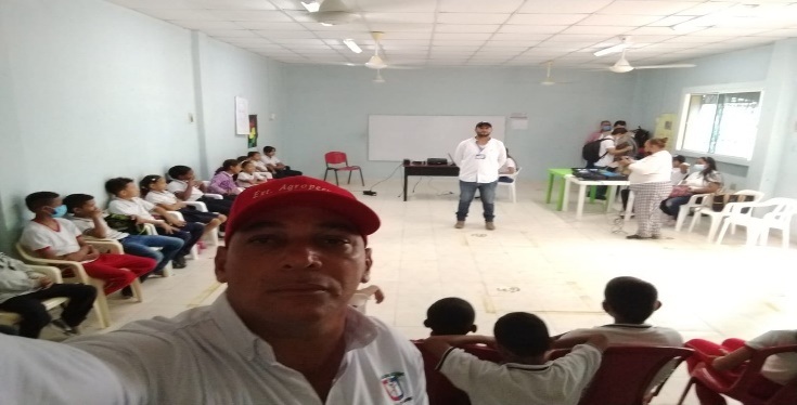 Capacitación grupal en salón comunitario con numerosos asistentes, técnico de AGRODASIN presentando