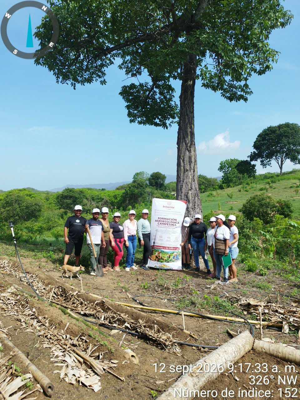 Grupo de participantes y equipo técnico posando junto a la valla informativa del proyecto, bajo un árbol grande